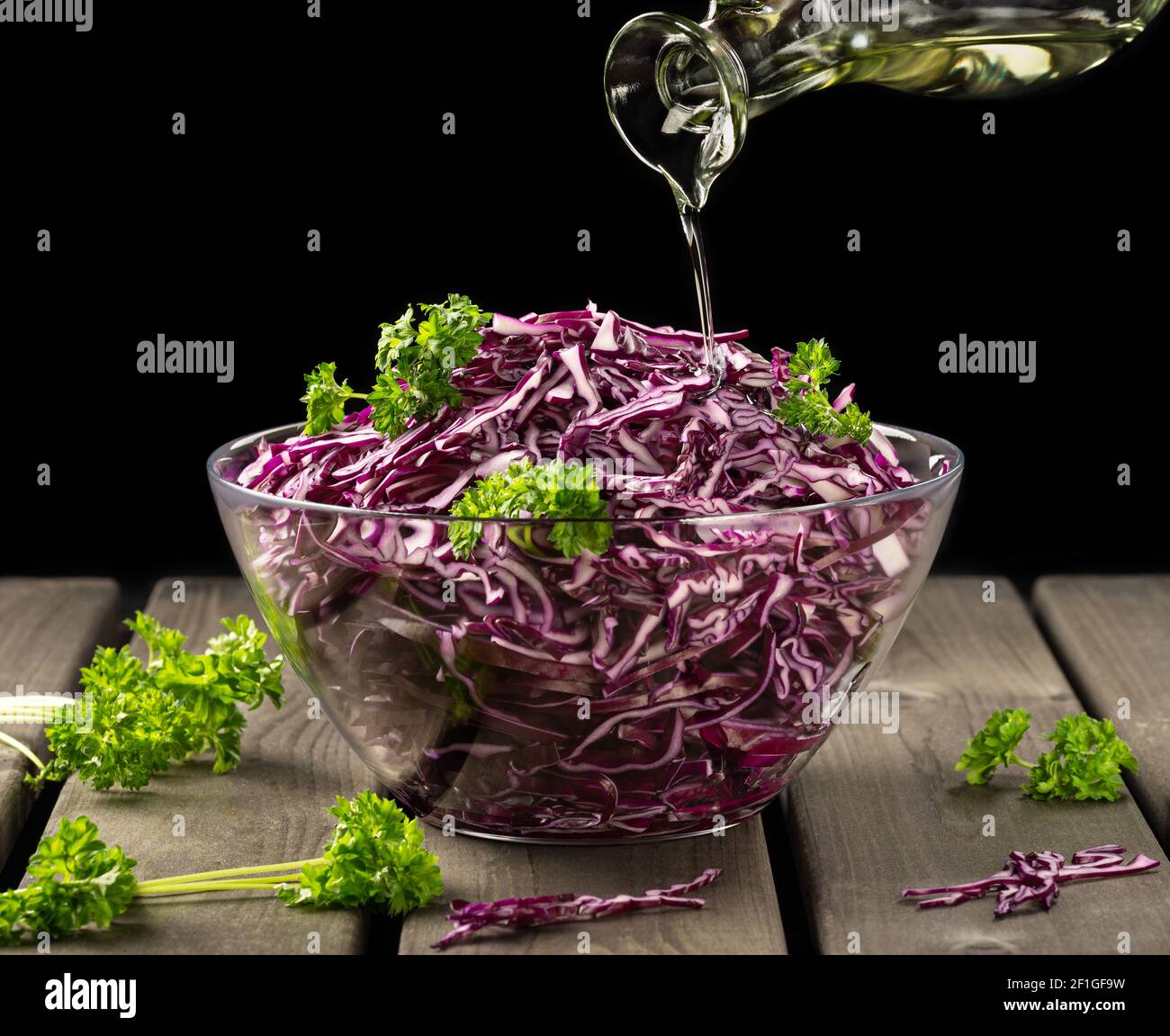 Veganes Konzept, gesunde Ernährung. Rotkohlsalat wird mit Olivenöl auf schwarzem Hintergrund gegossen, in einem rustikalen Stil, geringe Tiefenschärfe, selektiv Stockfoto