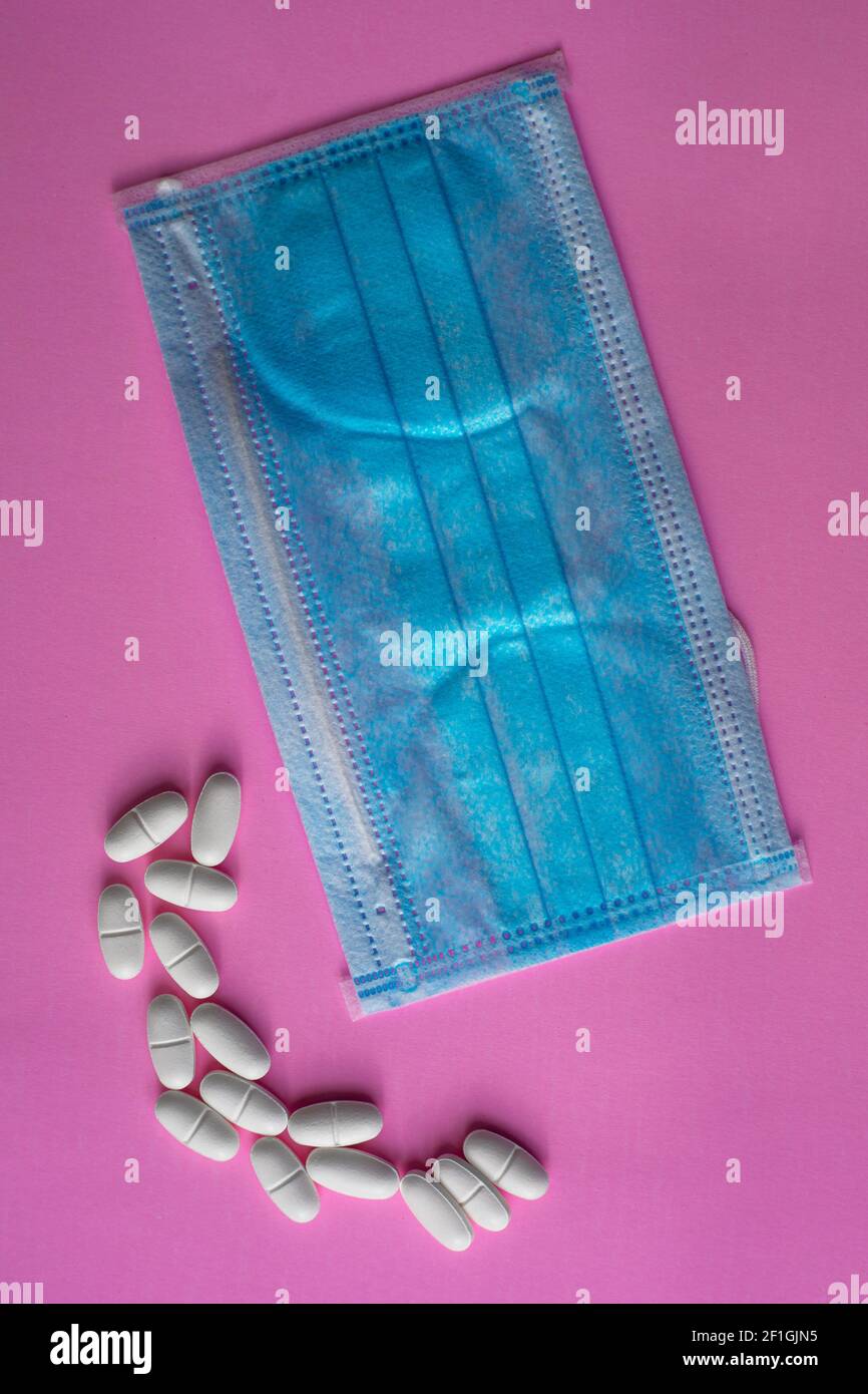 Medizinische blaue Schutzmaske und weiße Tabletten, Kapseln, Pillen oder Vitamine auf einem rosa Hintergrund Stockfoto