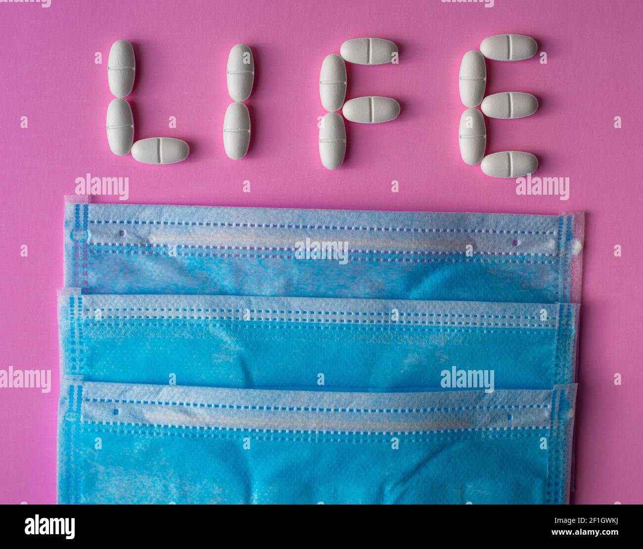 Medizinische blaue Schutzmasken und weiße, große Pillen, Tabletten oder Vitamine mit dem Text Leben auf einem rosa Hintergrund angeordnet Stockfoto