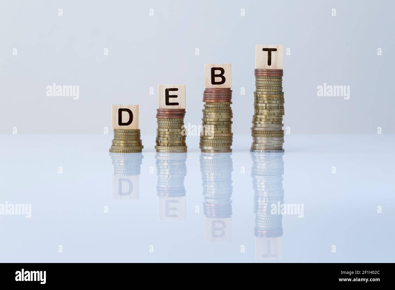 Wort „SCHULD“ auf Holzblöcken auf aufsteigenden Münzstapeln gegen Grau. Konzeptfoto von Investitionen, Finanzen, Unternehmen und mehr Darlehen. Stockfoto