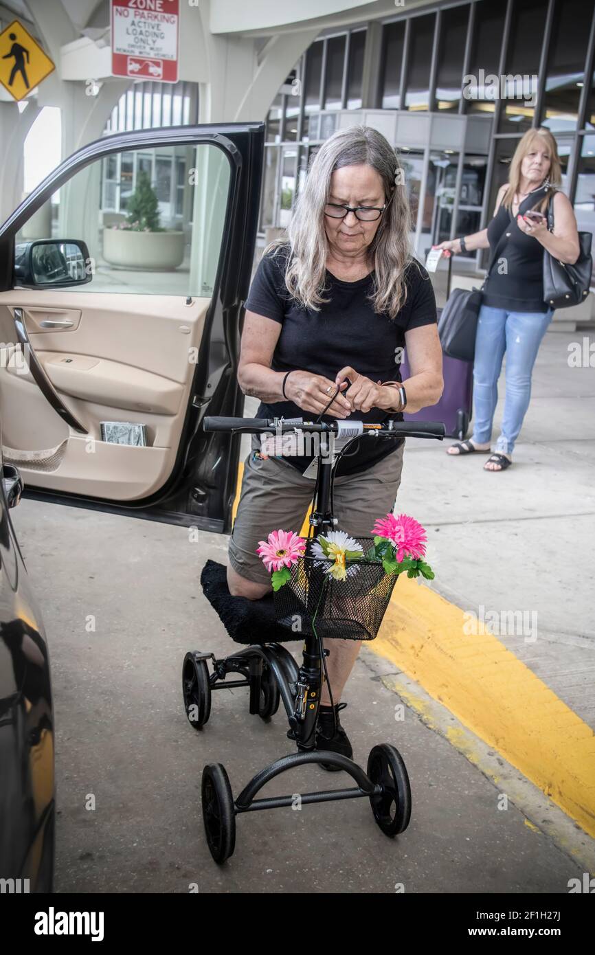 2019 05 20 Tulsa USA - Frau auf Mobilitätsroller mit Blumen Am Flughafen Abholzone durch offene Autotür mit einem anderen Frau mit Gepäck behind.jpg Stockfoto