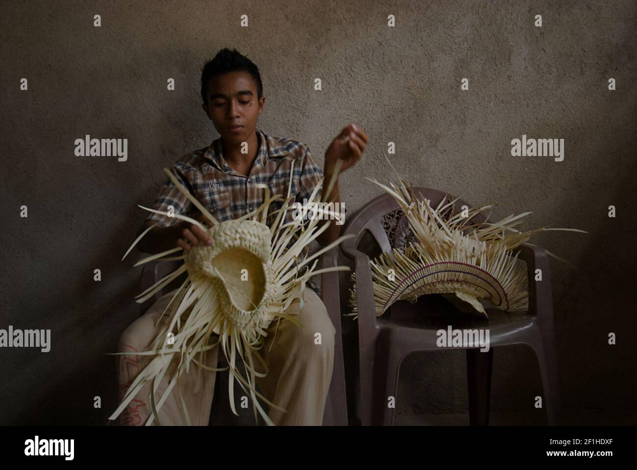 Ein junger Mann, der Lontar-Palmblätter verwendet, um den traditionellen Hut der Roten Insel, den Ti'i langga, in einem Produktionshaus auf der Roten Insel, Ost-Nusa Tenggara, Indonesien, zu machen. Stockfoto