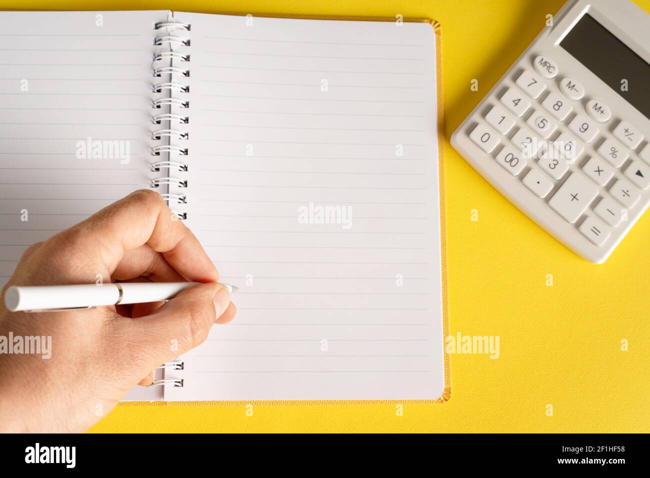 Nahaufnahme an der Hand halten Bleistift Schreiben auf Notizbuch von Der Rechner auf gelbem Hintergrund - Büro und Geschäft oder Zielkonzept Stockfoto