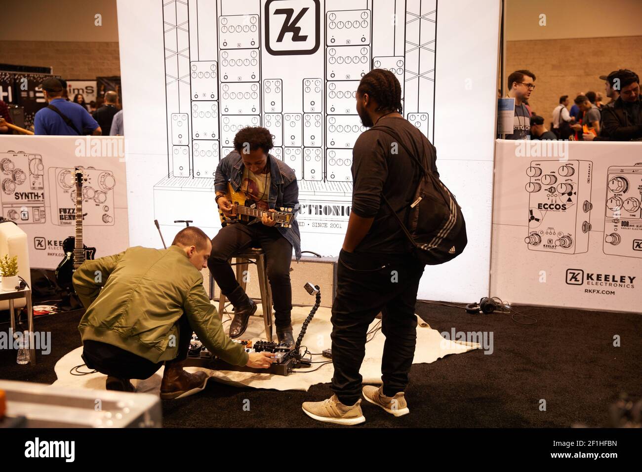 Schwarzer männlicher E-Gitarrist, der auf dem Hocker sitzt und Keeley spielt Gitarre Pedale auf Musical Instrument Convention Stockfoto