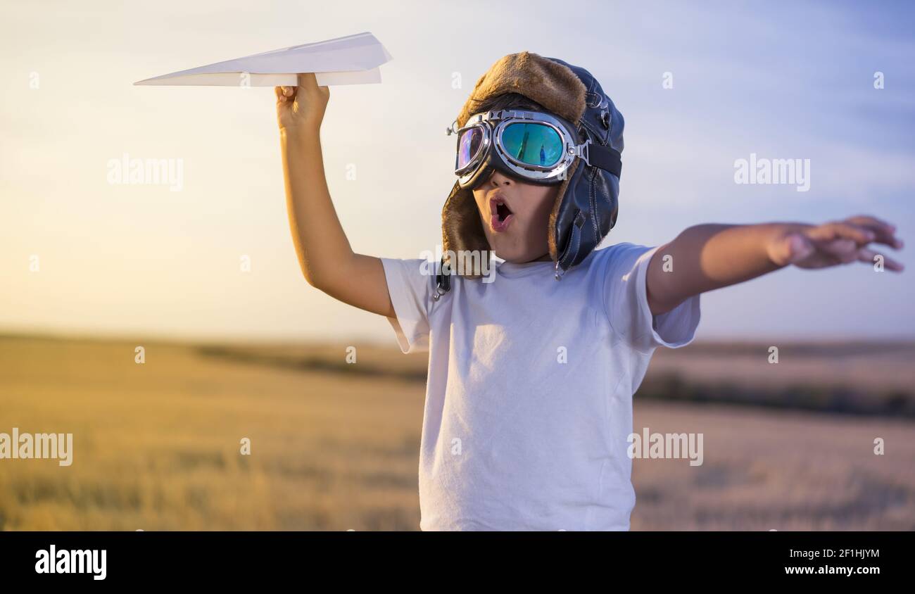 Spaß kleine Junge das Tragen von Helm und träumt davon, ein Aviator während der Wiedergabe eines Paper Plane bei Sonnenuntergang Stockfoto