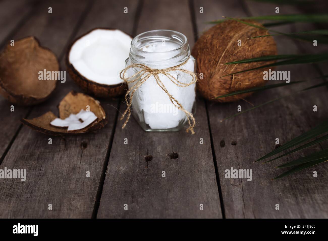 Gebrochene Kokosnüsse auf grauem Holzhintergrund mit Glas rohen Bio-Kokosnussöl extra vergine und Palmblatt. Weißes Kokosnusspulpe. Hochwertige Fotos Stockfoto