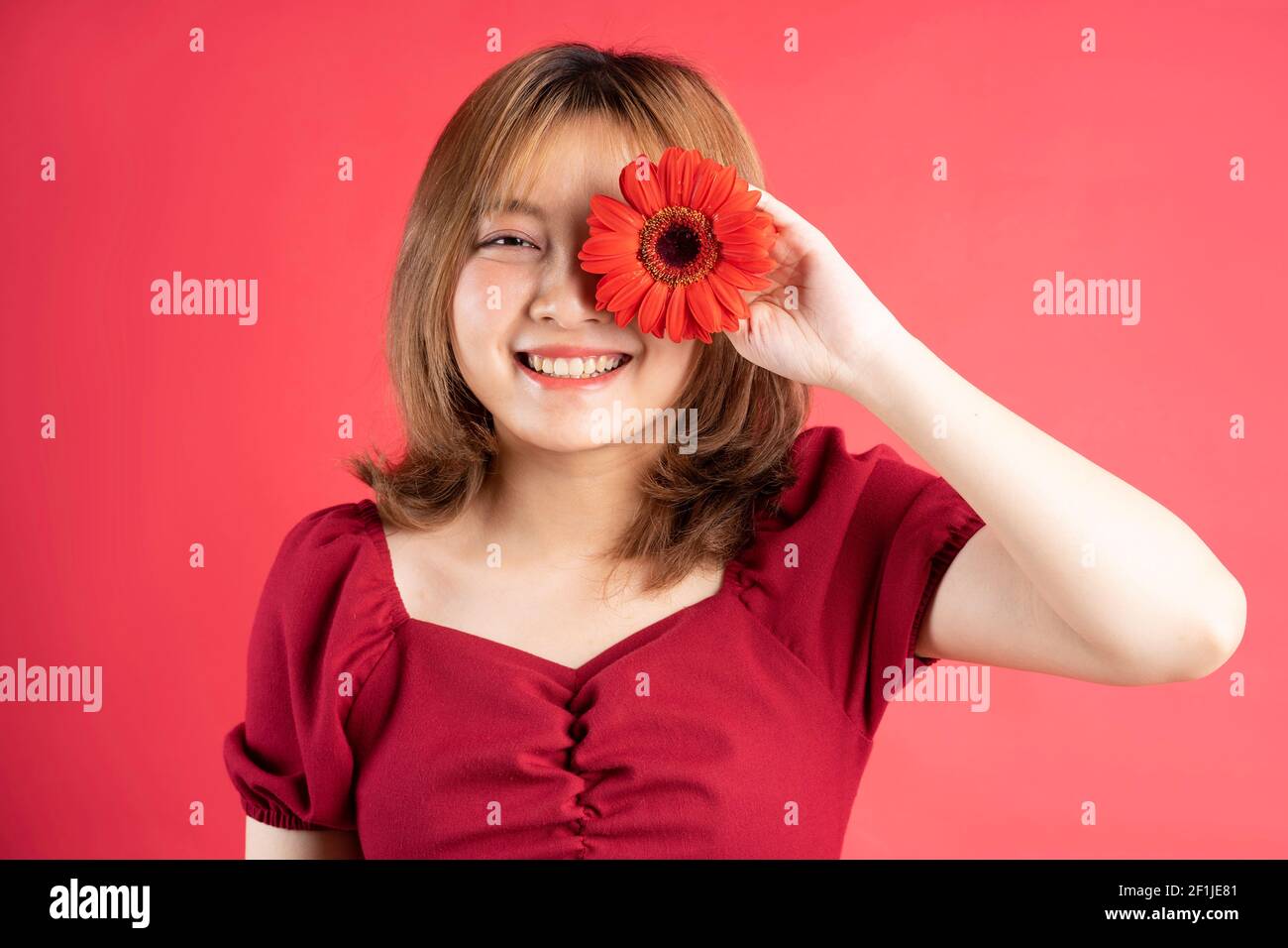 Das junge Mädchen hielt eine rote Gerbera Blume, die eine bedeckte Auge Stockfoto