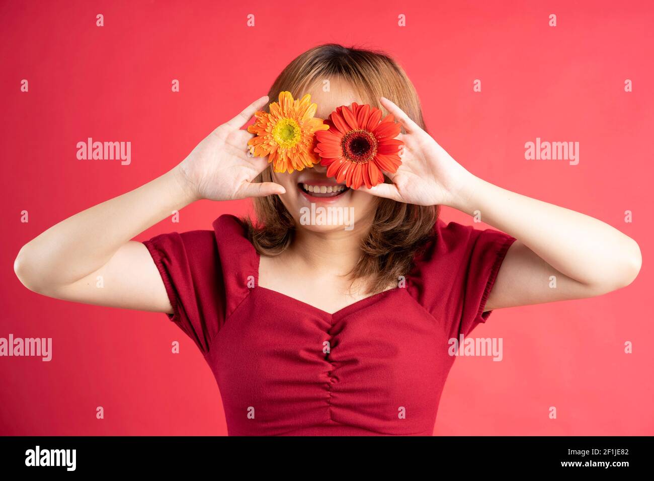 Junges Mädchen hält rote und gelbe Blume über sie gelegt Augen Stockfoto