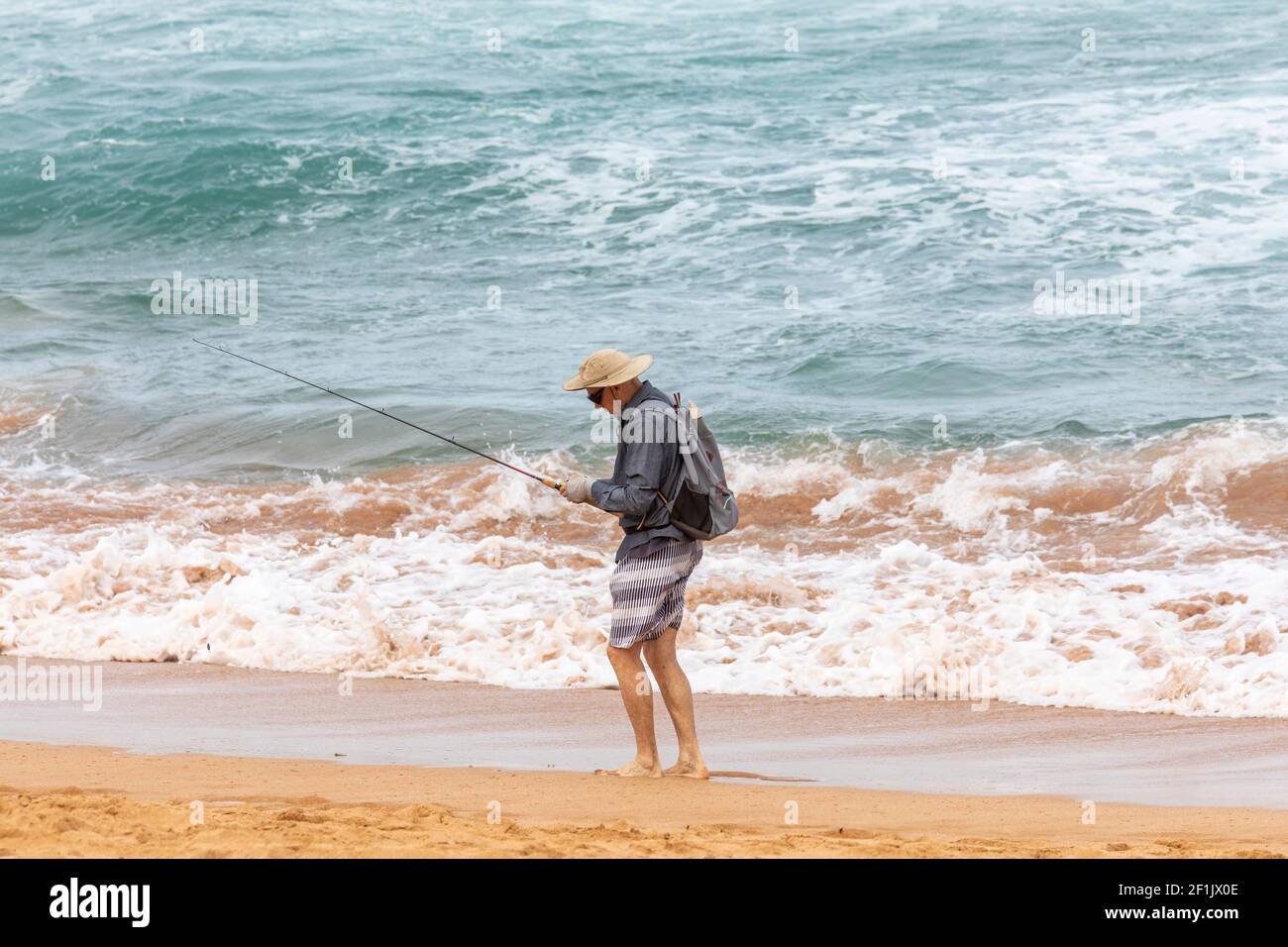 Strandangeln, ältere Männer, die an einem Strand in Sydney in Australien fischen, tragen Shorts und einen Hut Stockfoto