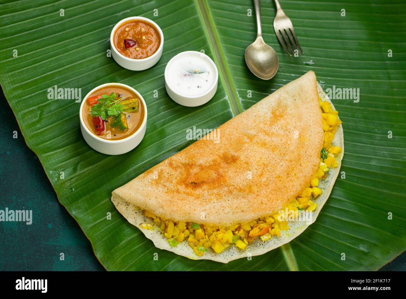 Dosa  Masala dosa, berühmtes südindisches Frühstückselement, das in einer Kasteneisernen Pfanne auf traditionelle Weise hergestellt und auf einem frischen Bananenblatt angeordnet wird. Stockfoto