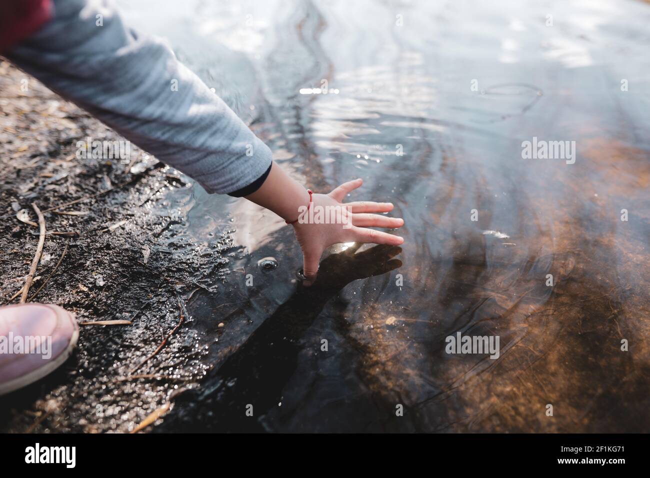 Geringe Schärfentiefe (selektiver Fokus) Details mit der Hand eines jungen Mädchens, das mit ihrer Hand im flachen Wasser eines Sees spielt. Stockfoto