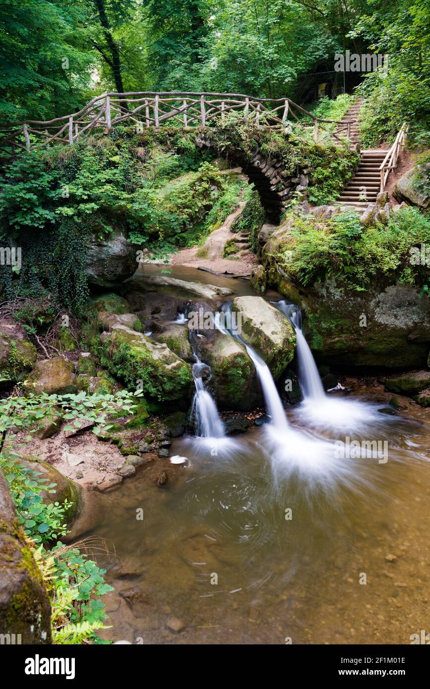 Idyllischer kleiner Wasserfall in üppig grüner Waldlandschaft mit einem Alte Brücke darüber Stockfoto