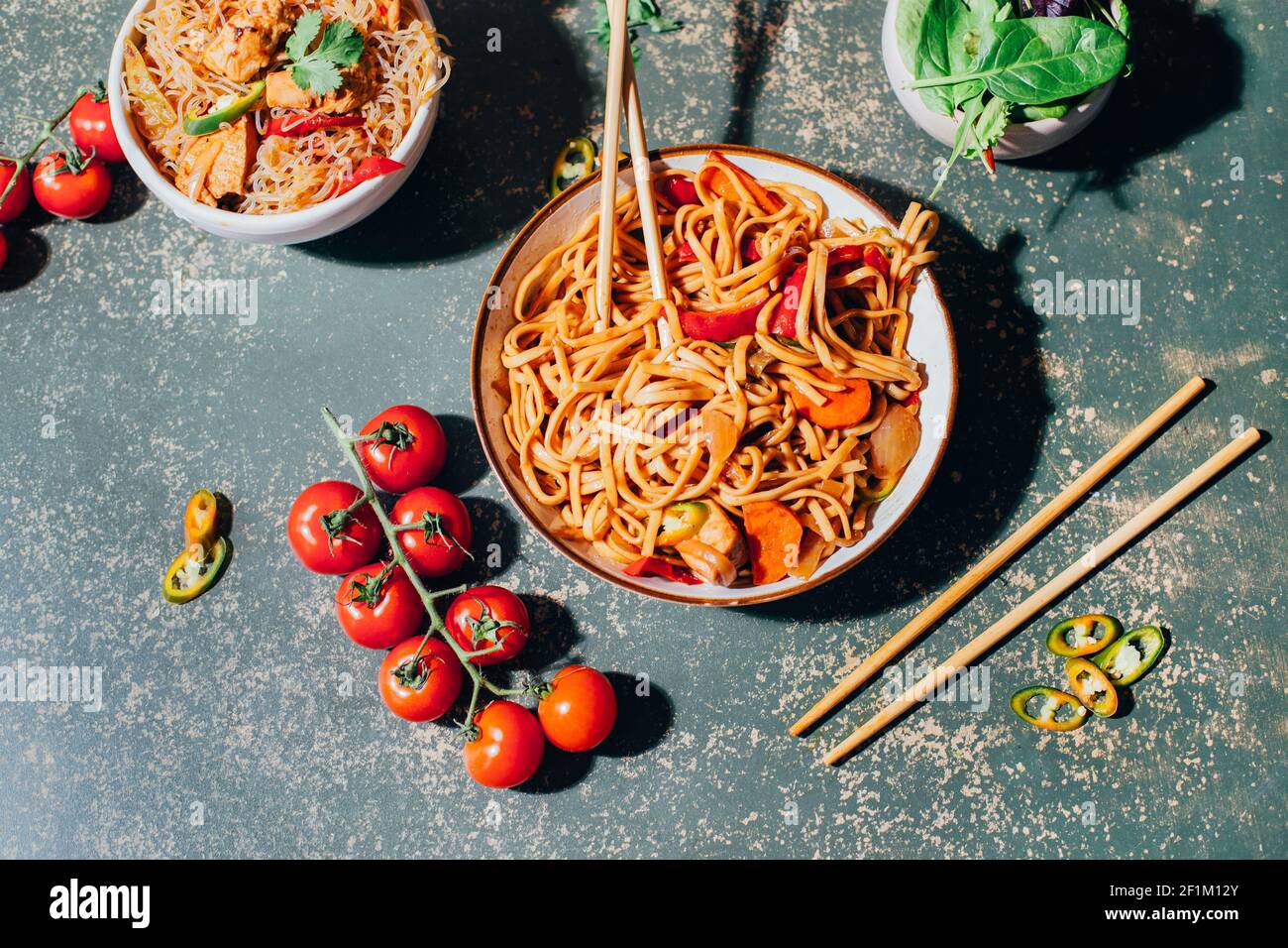 Nahaufnahme eines Tellers chinesischer Nudeln mit Fleisch und Gemüse in Tellern und chinesische Essstäbchen auf grünem Hintergrund Stockfoto