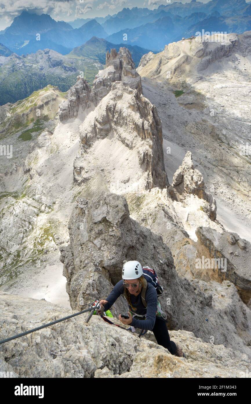 Coole junge attraktive Bergsteiger prüft ihr Handy, während Klettern auf einem Klettersteig in der D Stockfoto