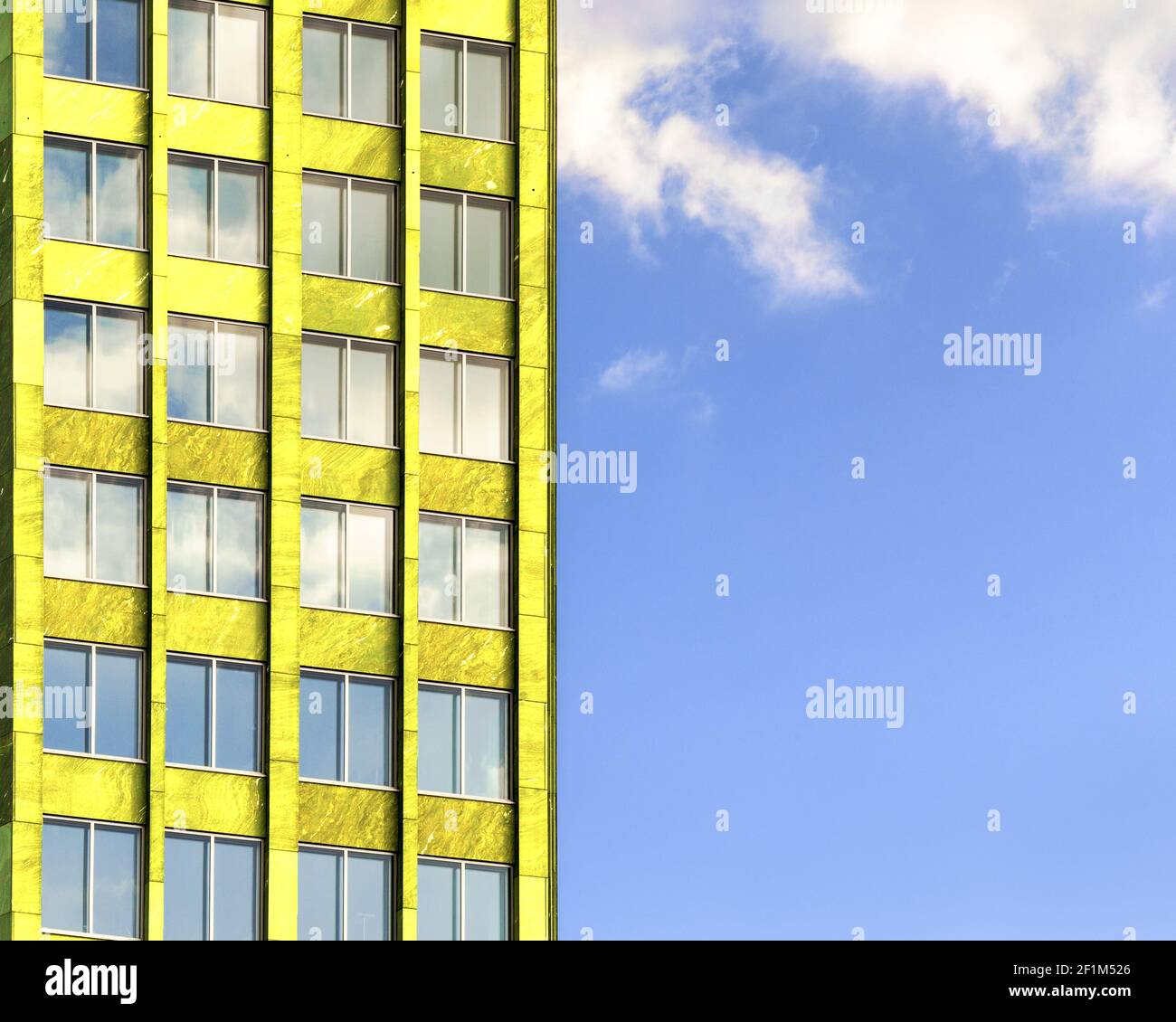 Fassade eines gelben Gebäudes mit Fenstern an einem blauen Himmel mit Wolken. Stockfoto