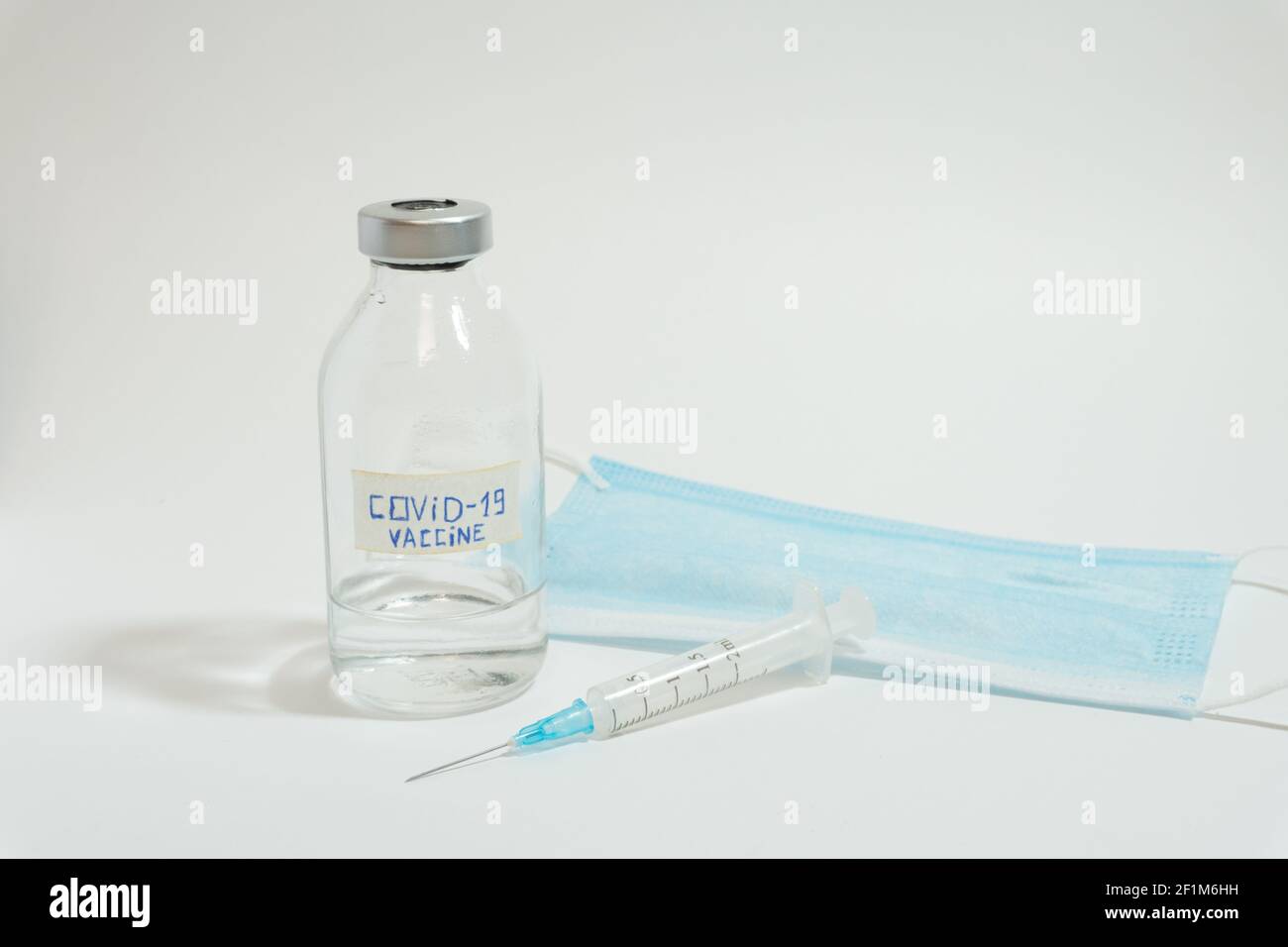 Coronavirus-Impfampulle, Einwegspritze und medizinische Gesichtsmaske Stockfoto