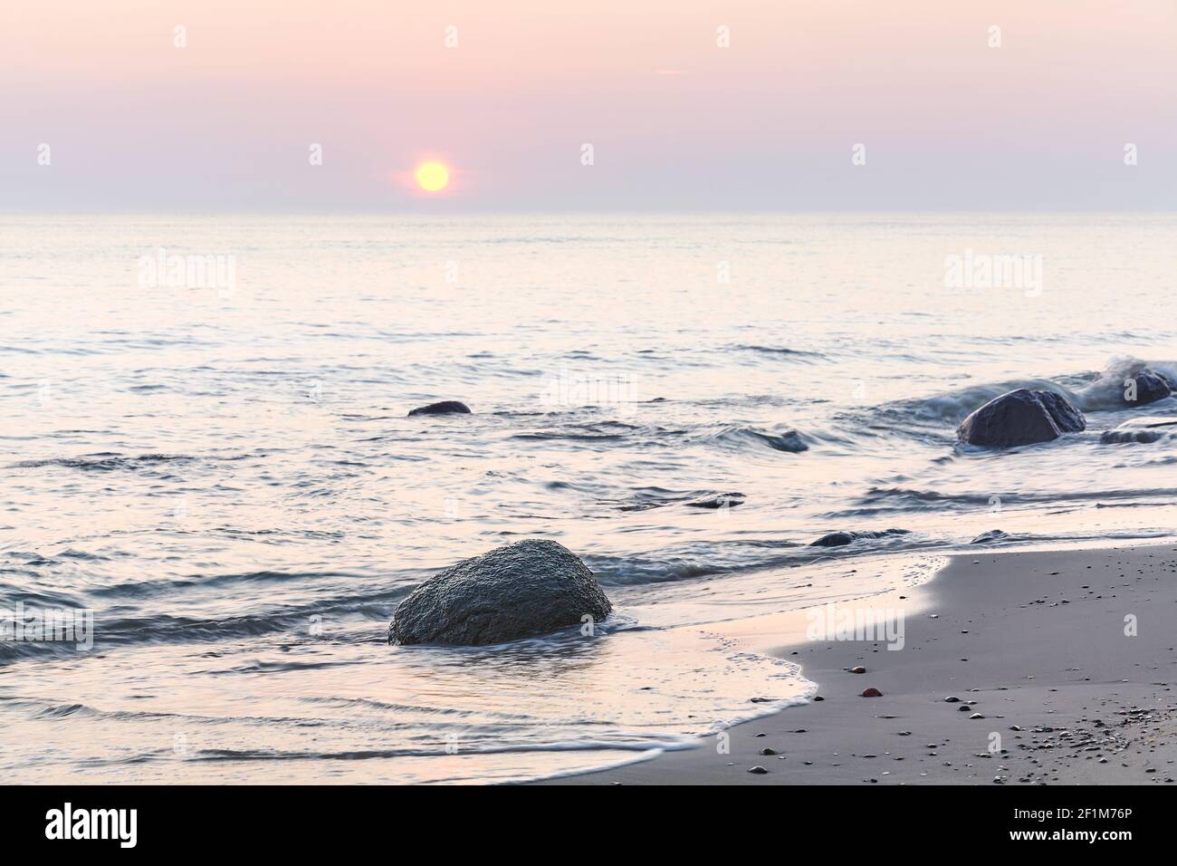 Friedlicher Sonnenaufgang am Strand, selektiver Fokus auf Felsen, Langzeitbelichtung. Stockfoto