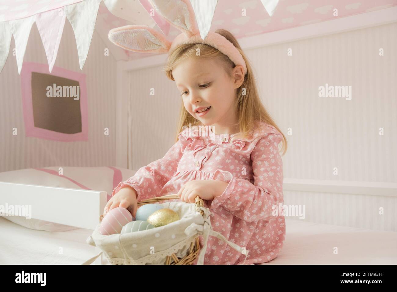 Kleines Mädchen mit Hasenohren und einem Korb mit Ostereiern. Frohe Ostern. Vorbereitung der Familie für Ostern. Osterhase Ohren.lächelndes Gesicht Stockfoto