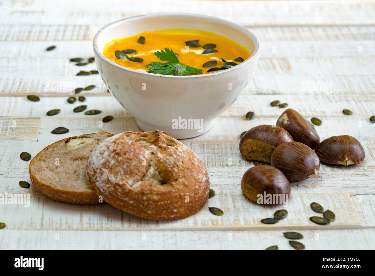 Bio-Kürbissuppe in einer weißen Schale umrahmt von Kastanien Und Kastanienbrot und Kürbiskerne Stockfoto