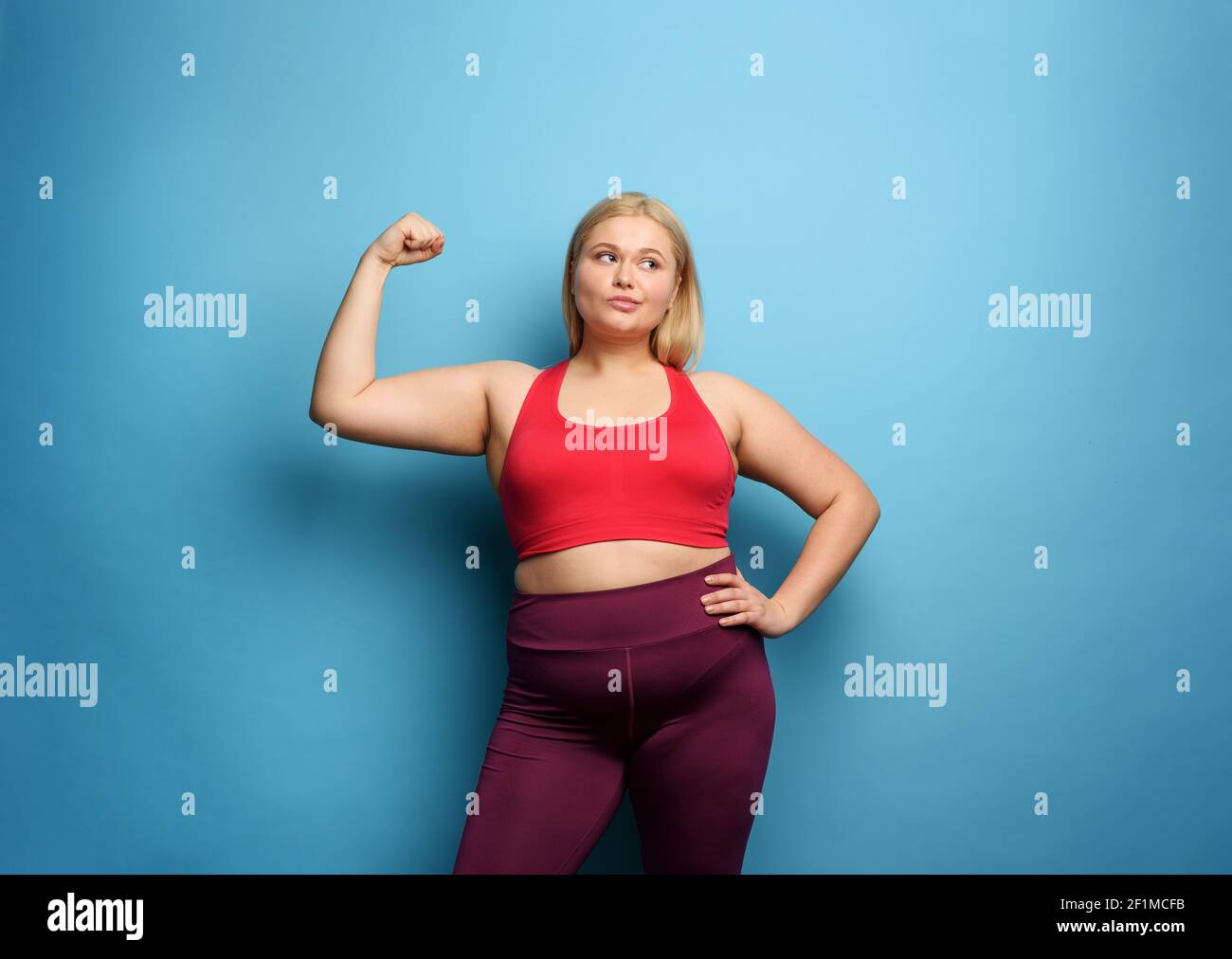 Fat Mädchen tut Fitness-Studio zu Hause. Nachdenklicher Ausdruck. Cyanfarbener Hintergrund Stockfoto