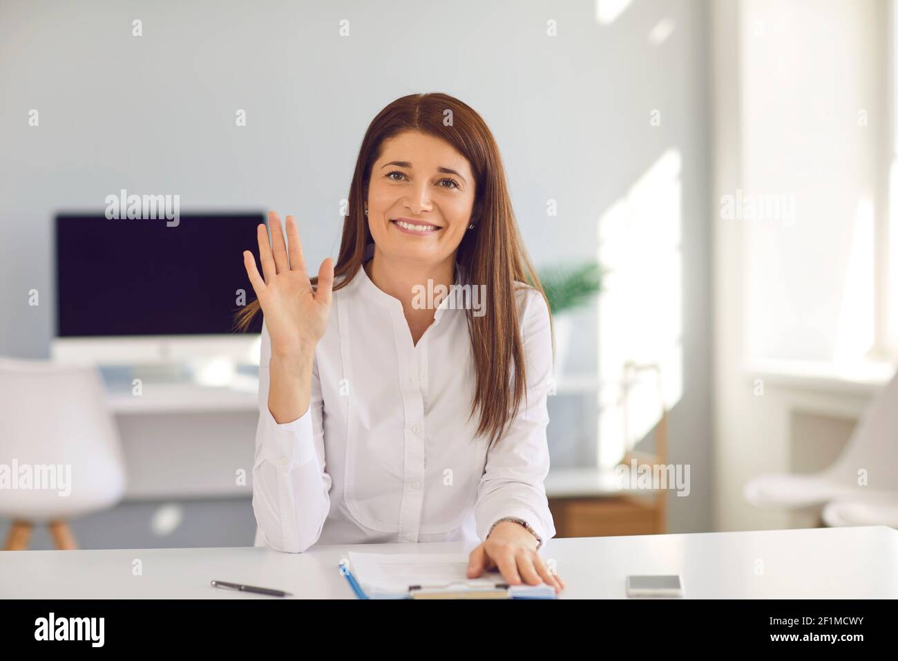 Junge Geschäftsfrau und Influencer winken Hand an Kamera Gruß Teilnehmer in Online-Meeting. Stockfoto