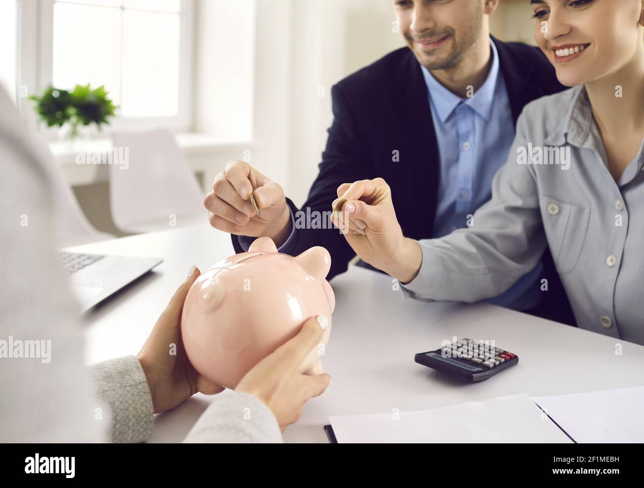 Ein Paar legt Münzen in ein Sparschwein, das am Schreibtisch sitzt bankmanager oder Versicherungsmakler Stockfoto