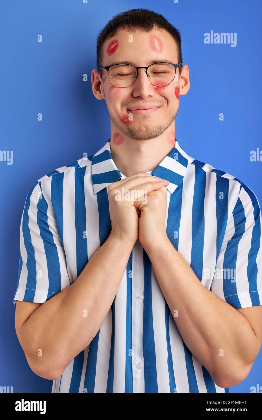 Romantisches Porträt von jungen kaukasischen Nerd mit Kuss Abdrücke isoliert auf blauem Hintergrund, glücklich Kerl verlieben sich in jemanden, stehen in guter Laune. peo Stockfoto Romantisches Porträt von jungen kaukasischen Nerd mit Kuss Abdrücke isoliert auf blauem Hintergrund, glücklich Kerl verlieben sich in jemanden, stehen in guter Laune. peo Stockfoto
