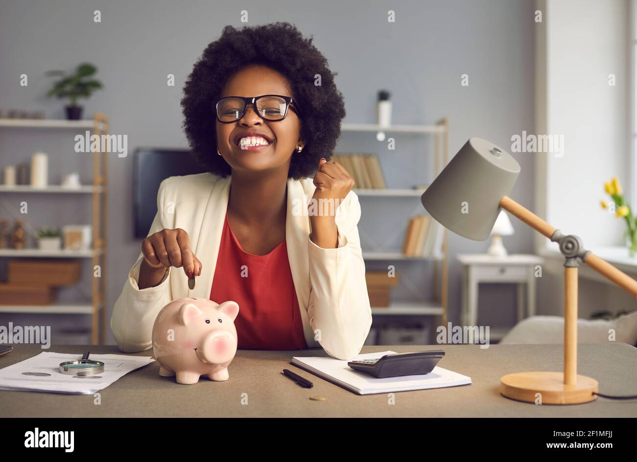Aufgeregt glücklich afroamerikanische Frau mit ja Geste setzen Münze Im Sparschwein Stockfoto