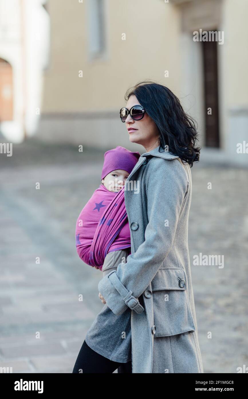 Portrait von trendigen Babytragen Mutter trägt ihr Kind in der Stadt Stockfoto
