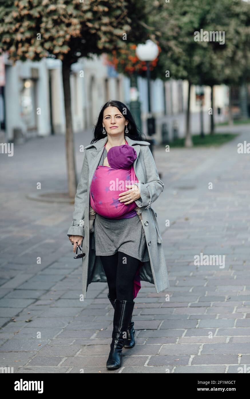 Porträt von trendigen Babytragemutter zu Fuß in der Stadt Stockfoto