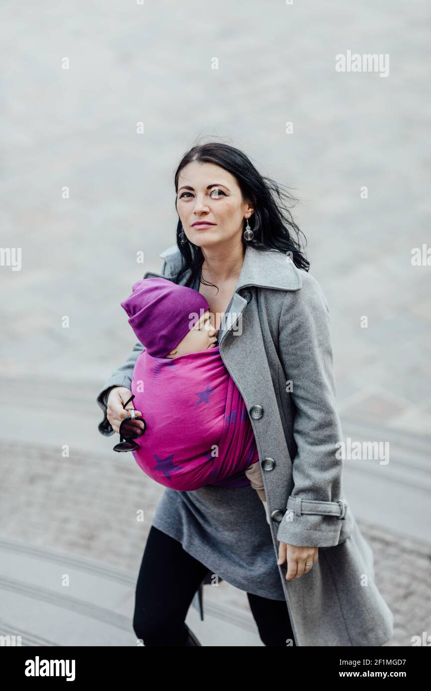 Portrait der trendigen Babytragemutter trägt ihr schlafendes Kind in Die Stadt Stockfoto