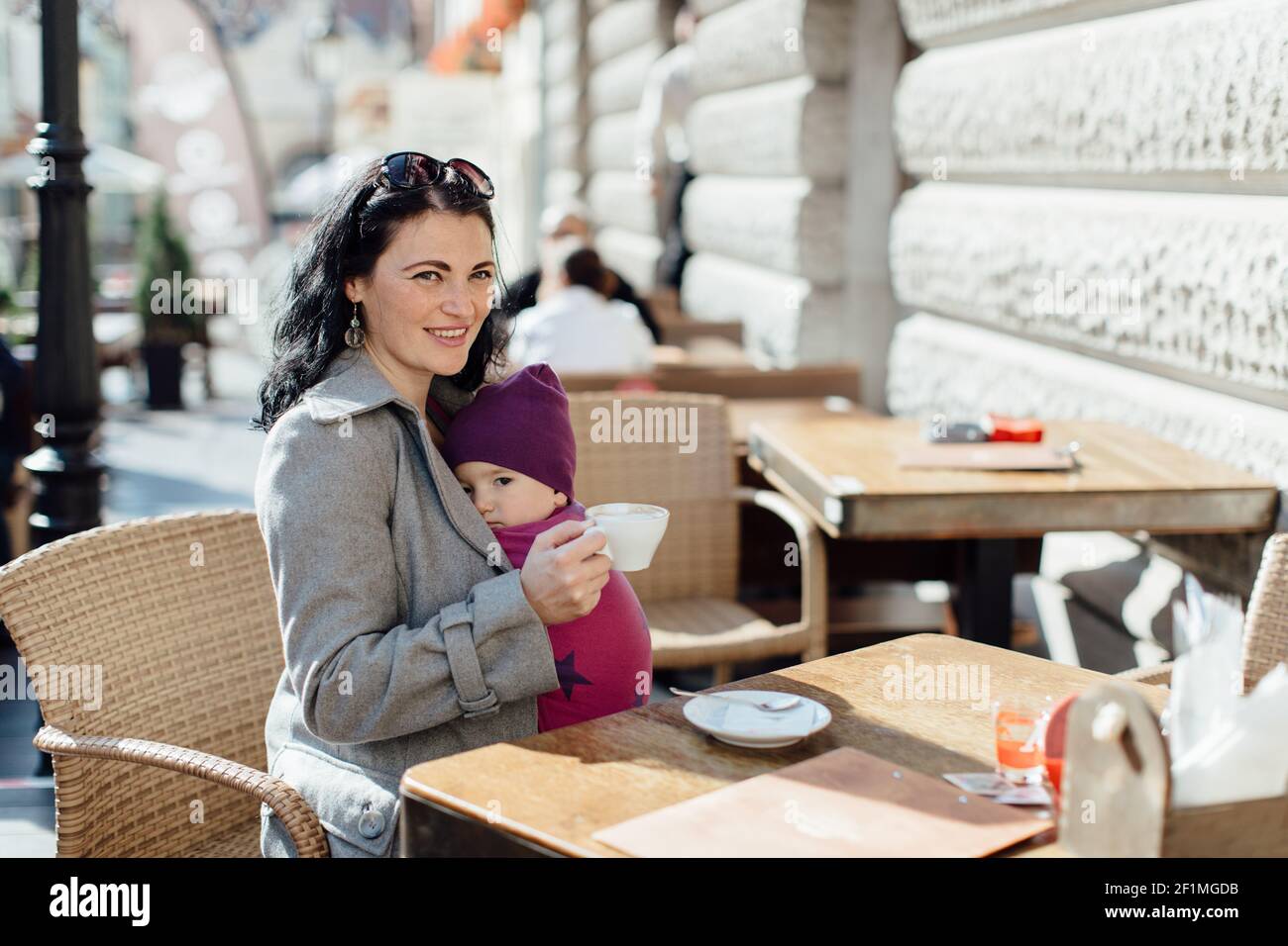 Portrait der trendigen Babytragemutter trägt ihr Kind in gewebt Im Café einwickeln Stockfoto