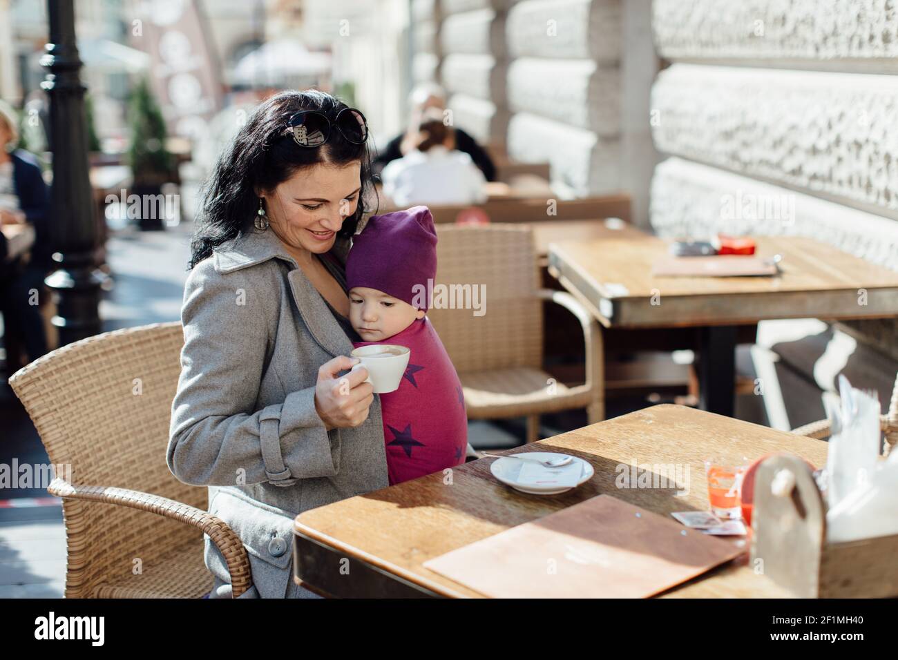 Portrait der trendigen Babytragemutter trägt ihr Kind in gewebt Im Café einwickeln Stockfoto