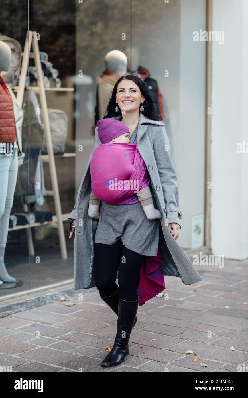 Portrait von glücklichen Babytragemutter trägt ihr Kind vorbei Schaufenster Stockfoto