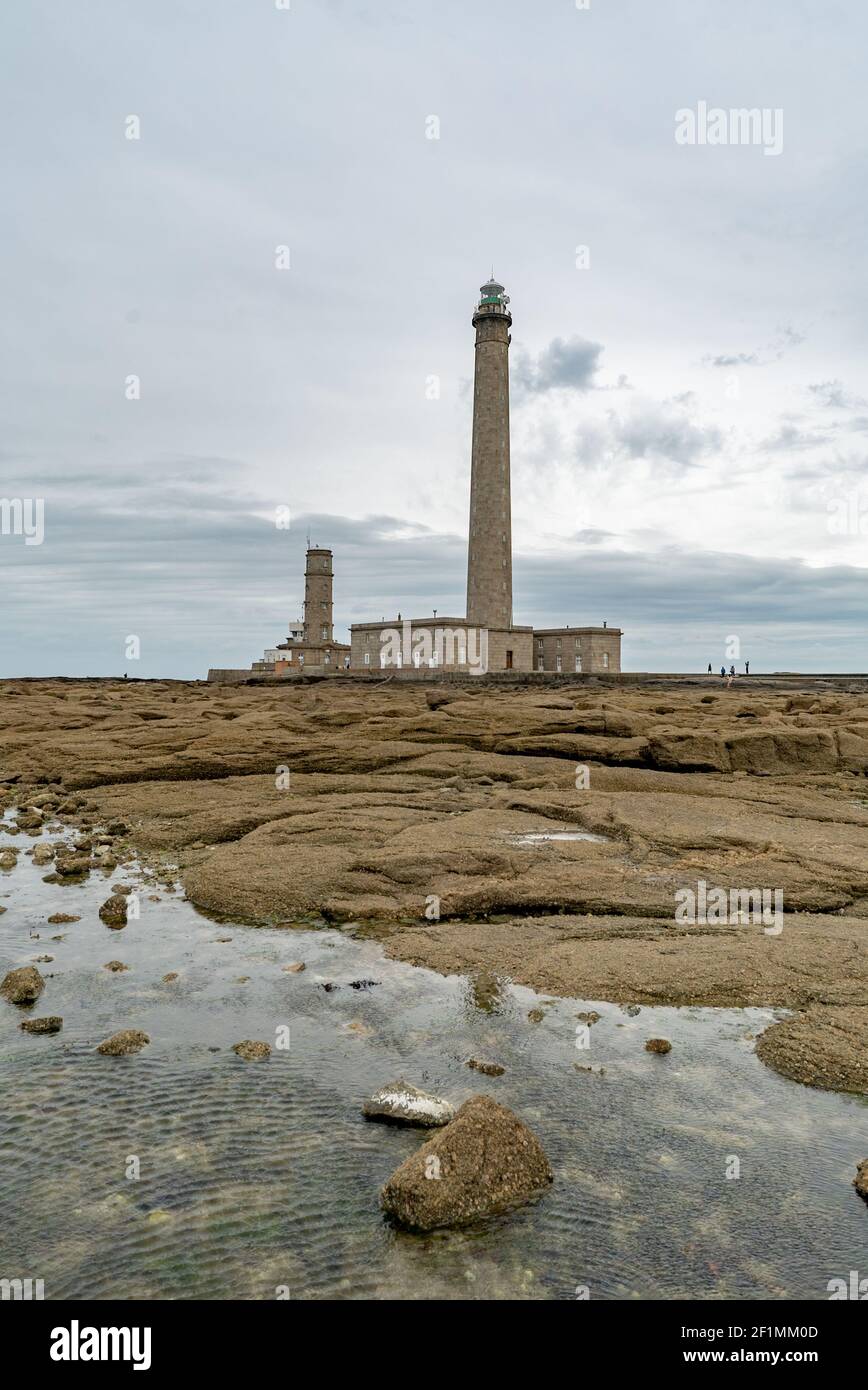 Hoher Leuchtturm aus Stein mit felsigen Gezeitenbecken am Ufer im Vordergrund Unter stürmischem Himmel Stockfoto