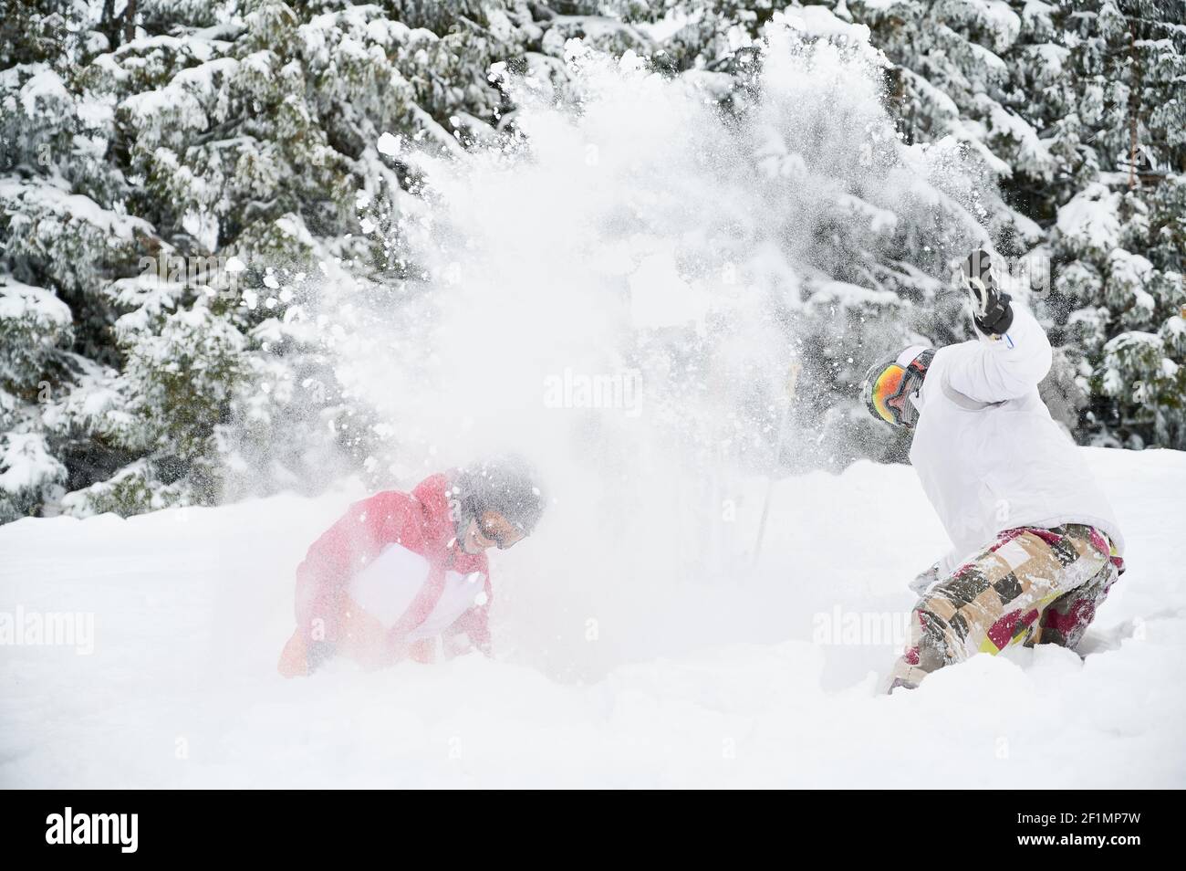 Paar Skifahrer in Skianzügen werfen frischen Pulverschnee hoch in der Luft und lächeln, gute Zeit mit schönen verschneiten Bäumen im Hintergrund. Konzept der Wintersport-Aktivitäten, Spaß und Beziehungen. Stockfoto