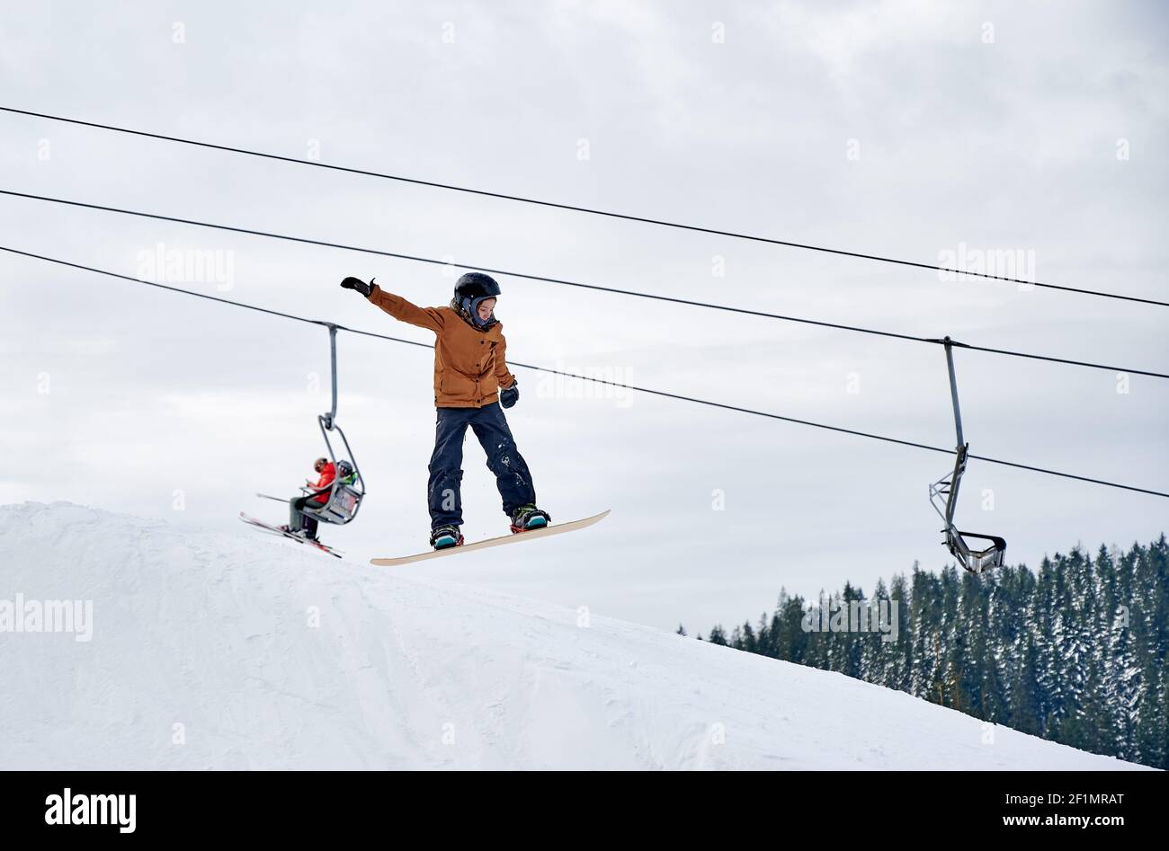 Snowboarder macht Tricks in den Bergen in der Wintersaison, hoch fliegen mit Snowboard gegen Sessellift und bewölkten Himmel. Low-Angle-Ansicht. Konzept der Winter Arten von Sport, Extremsport. Stockfoto