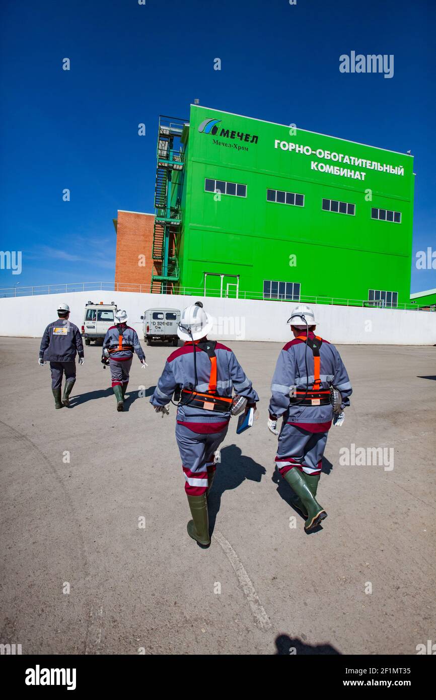 Khromtau, Region Aktobe, Kasachstan - Mai 06 2012: Gruppe von Bergleuten in weißen Harthüten gehen in die grüne Konzentrationsanlage (Verarbeitungsanlage) Gebäude Stockfoto
