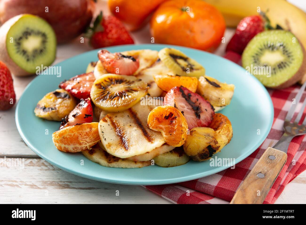 GEGRILLTES OBST auf einem blauen Teller und weißem Holzhintergrund Stockfoto