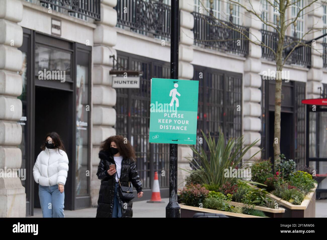 Frauen, die an A vorbeiziehen Bitte halten Sie Ihre Wegweiser auf Regents Street London während der Coronavirus-Sperre tragen PPE-Masken unter Leere Geschäfte Stockfoto