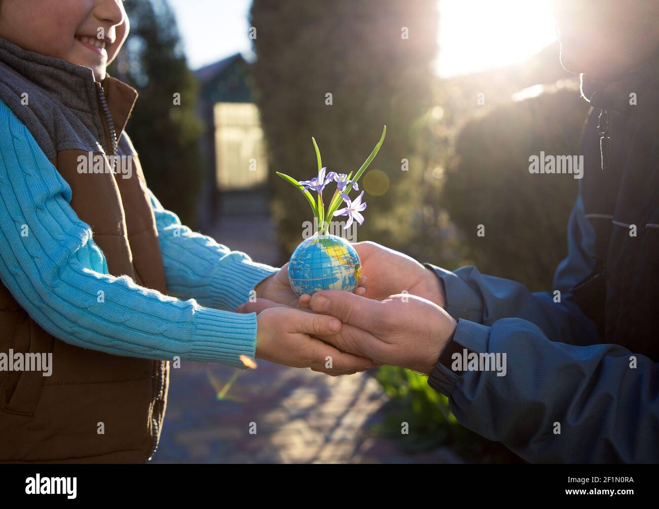 In den Händen von Kind und Mann, Vater und Sohn ist Erde in Miniatur, eine kleine Kugel in Form eines Globus, aus dem kleine Blumen wachsen. Earth Day Konzept, Ec Stockfoto