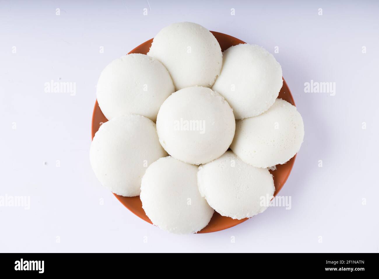 Idly oder Idli, südindisches Hauptfrühstück, das wunderschön in einem irdenen Geschirr mit weißem Hintergrund angeordnet ist. Stockfoto