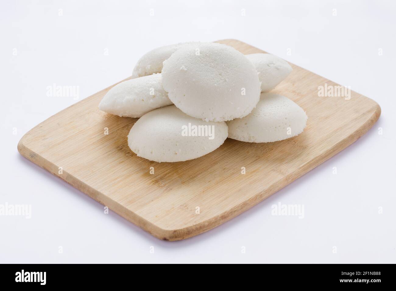 Idly oder Idli, südindisches Hauptfrühstück, das wunderschön auf einem Holzsockel mit weißem Hintergrund angeordnet ist. Stockfoto