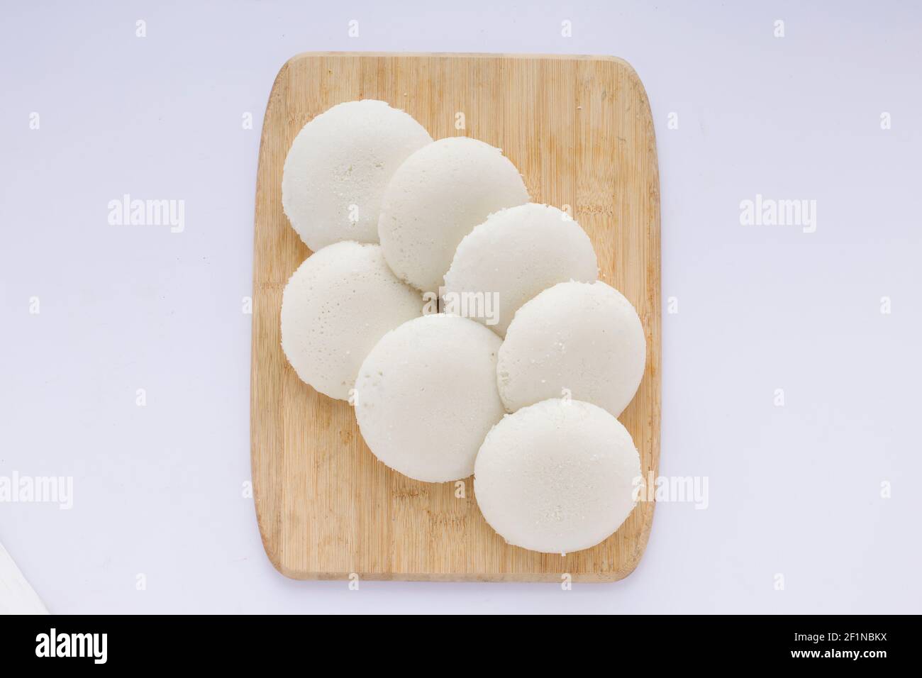 Idly oder Idli, südindisches Hauptfrühstück, das wunderschön auf einem Holzsockel mit weißem Hintergrund angeordnet ist. Stockfoto