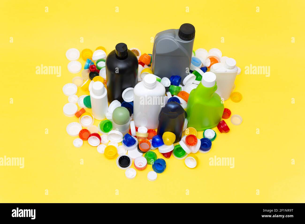 Verschiedene Kunststoffbehälter in verschiedenen Größen und Formen und viele Kappen isoliert auf gelbem Hintergrund. Recyclingkonzept. Leerzeichen für Text. Stockfoto