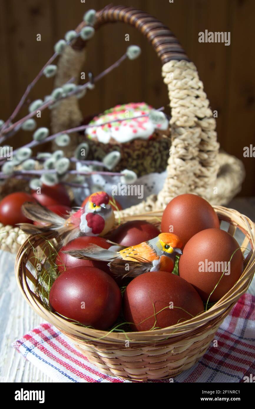 Spielzeugvögel sitzen in einem Weidenkorb auf bemalten Eiern. Im Mittelpunkt der Kuchen- und Weidenzweige. Stockfoto