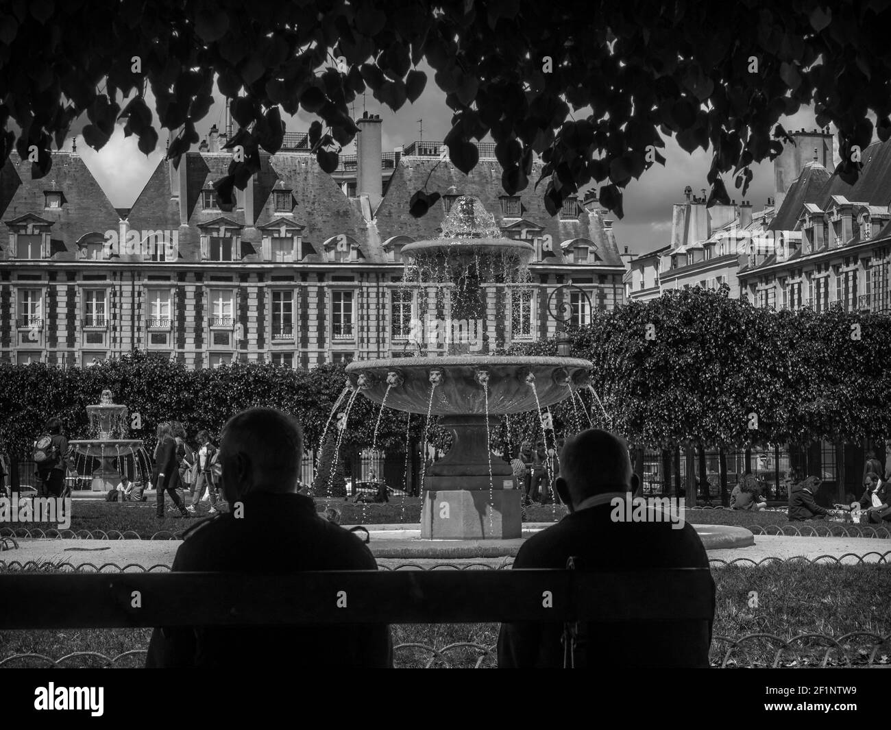 Zwei Männer entspannen sich in einem Pariser Park und beobachten den Brunnen und die Menschen. Stockfoto
