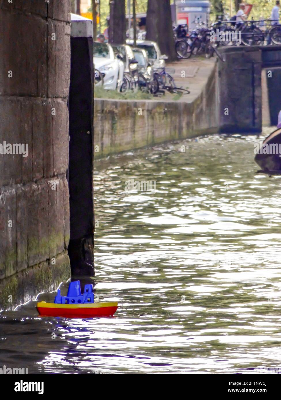 Ein kleines Plastikspielzeugboot in roten, blauen und gelben Farben, das in einem Wasserkanal in Amsterdam verloren gegangen ist. Stockfoto