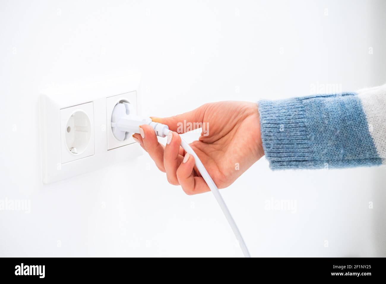 Kabel von Hand in die Buchse an der weißen Wand stecken Stockfoto