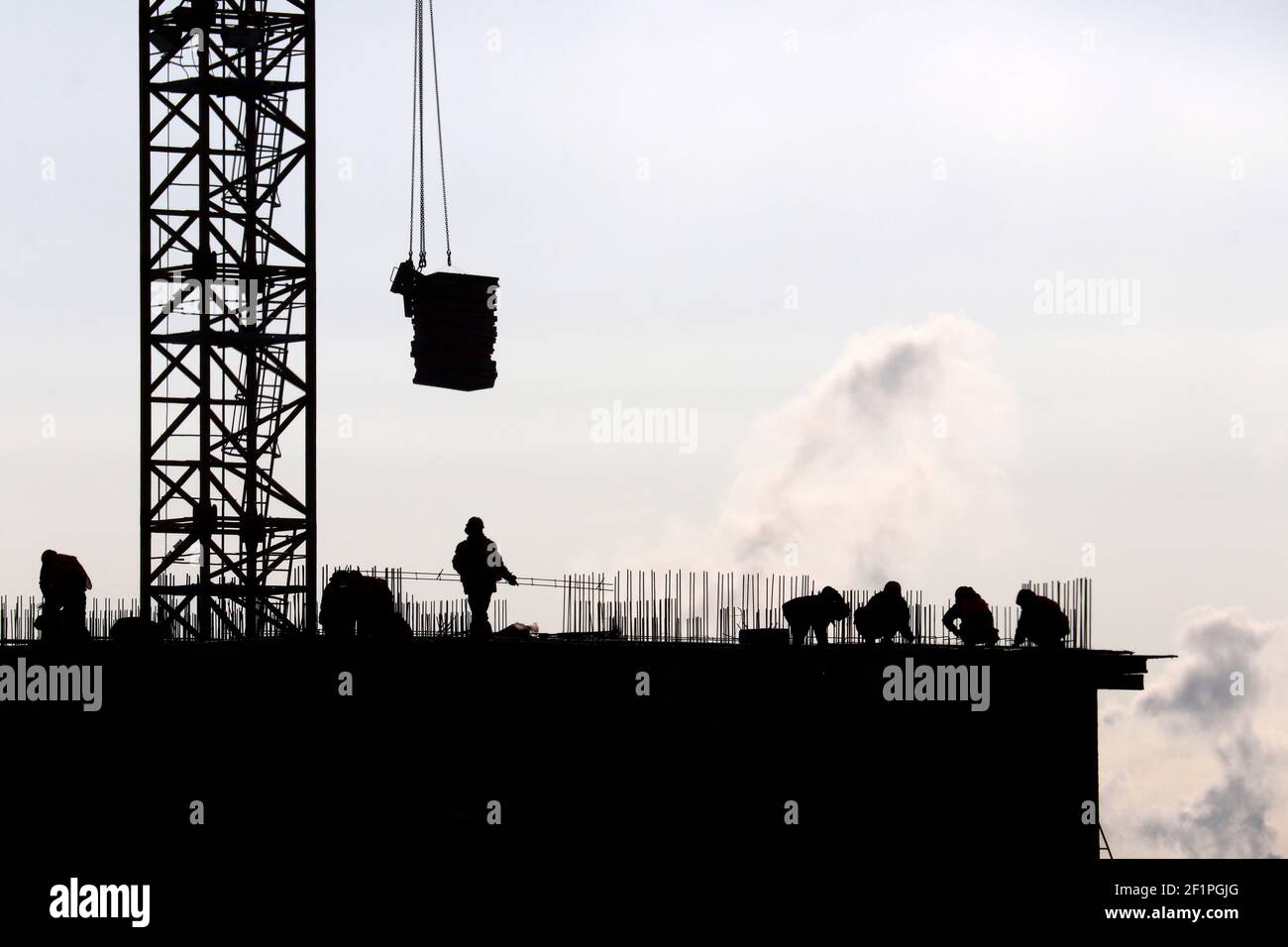 Silhouetten von Arbeitern und Baukran mit Ladung gegen den Himmel. Wohnungsbau, Bauherren arbeiten auf Gerüsten Stockfoto